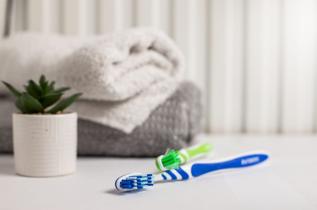 closeup of two toothbrushes  on a table next to towels and a plant